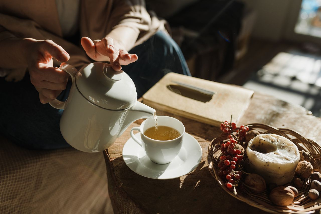 Derramando chá quente lentamente em uma xícara de cerâmica rústica - slow living