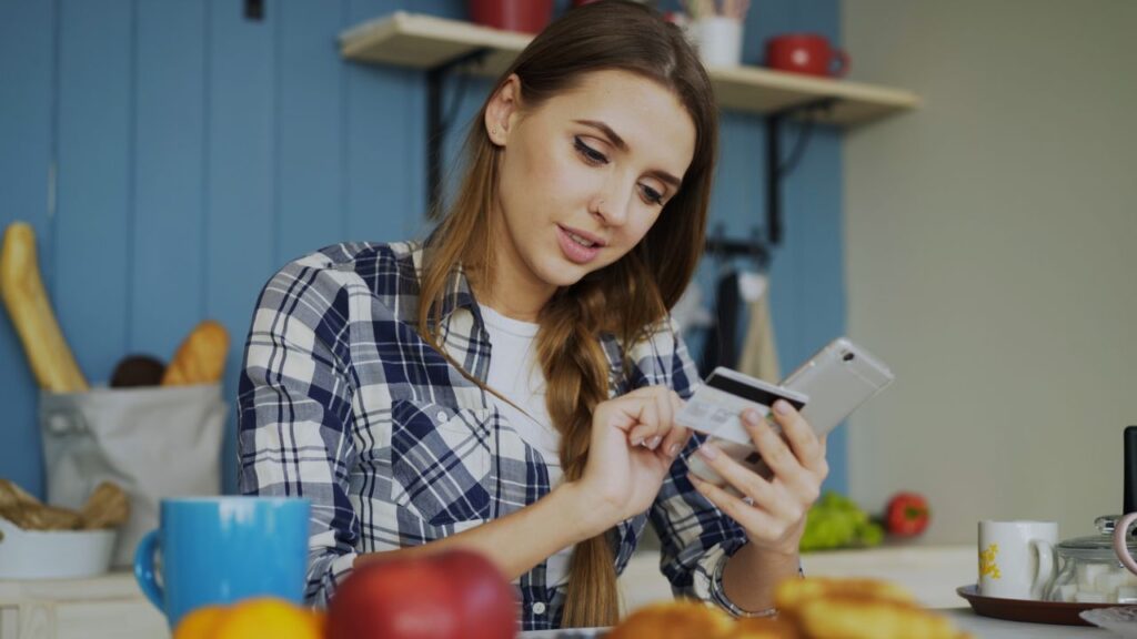 Mulher fazendo compras no celular com o cartão de crédito na mão - compras por impulso