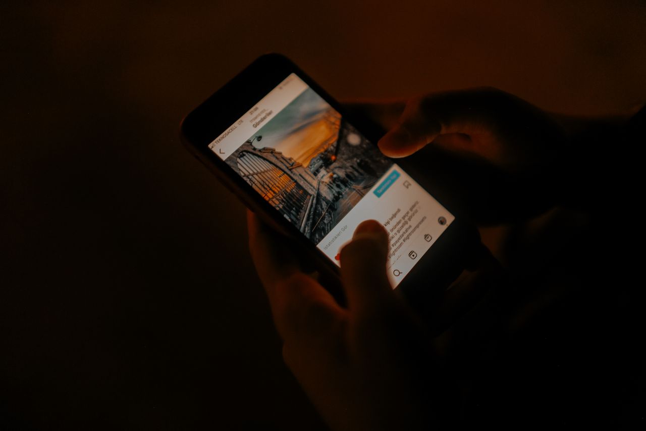 Pessoa segurando o celular brilhando em um quarto escuro - ansiedade de informação