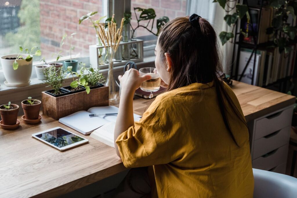 economia da atenção - Uma cena tranquila de uma mesa minimalista ao lado de uma janela, com pouquíssimos elementos um livro ou bloco de notas, uma planta e uma xícara, banhada por luz natural
