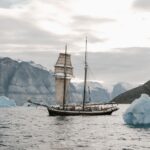 a arte de falhar e recomeçar - Um navio cargueiro ou veleiro cercado por imensas placas de gelo e montanhas gélidas sob um céu dramático e frio