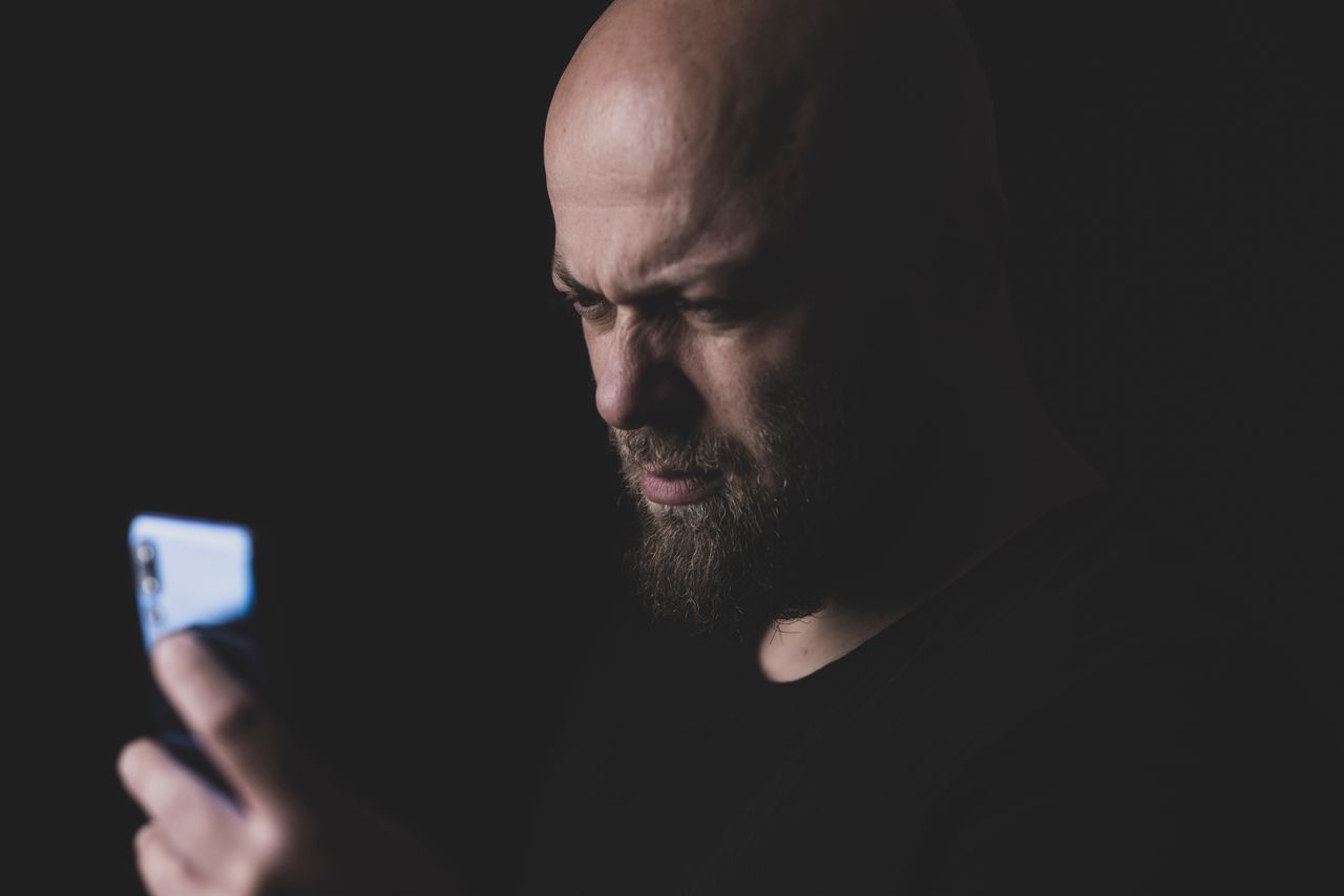 sindrome do pensamento acelerado - Uma pessoa segurando o celular em um ambiente com luz suave ou penumbra, com o rosto levemente iluminado pela tela e uma expressão de cansaço ou sobrecarga