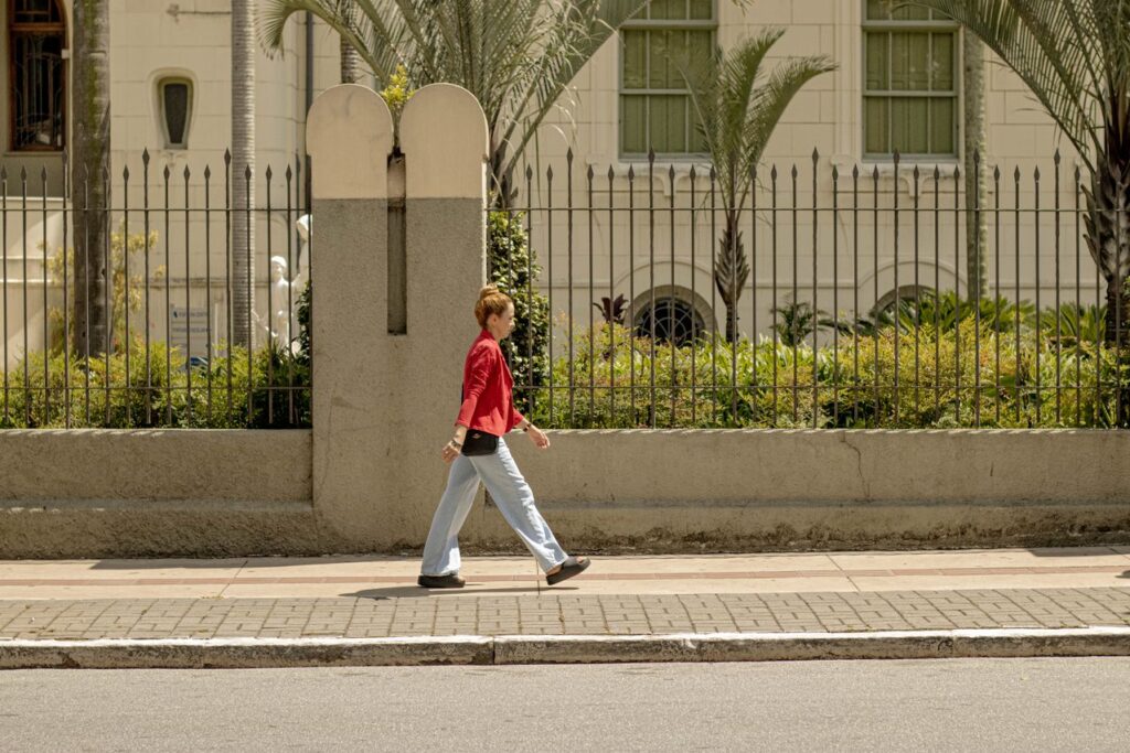 recomeçar na vida adulta - Uma pessoa caminhando tranquilamente ao ar livre com uma expressão leve e confiante, cercada por elementos naturais ou arquitetura urbana acolhedora