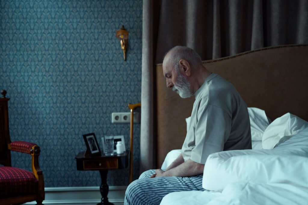 história inspiradora de Arthur Croft - homem de meia-idade sentado na beira da cama em um quarto simples e de iluminação baixa, em tom reflexivo
