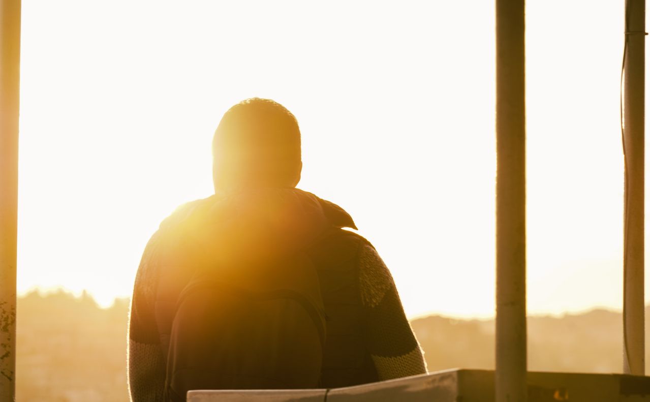 como começar bem o dia - pessoa na varanda, quintal ou em frente a uma janela aberta, banhada pela luz dourada do amanhecer, transmitindo a sensação de um despertar calmo e intencional