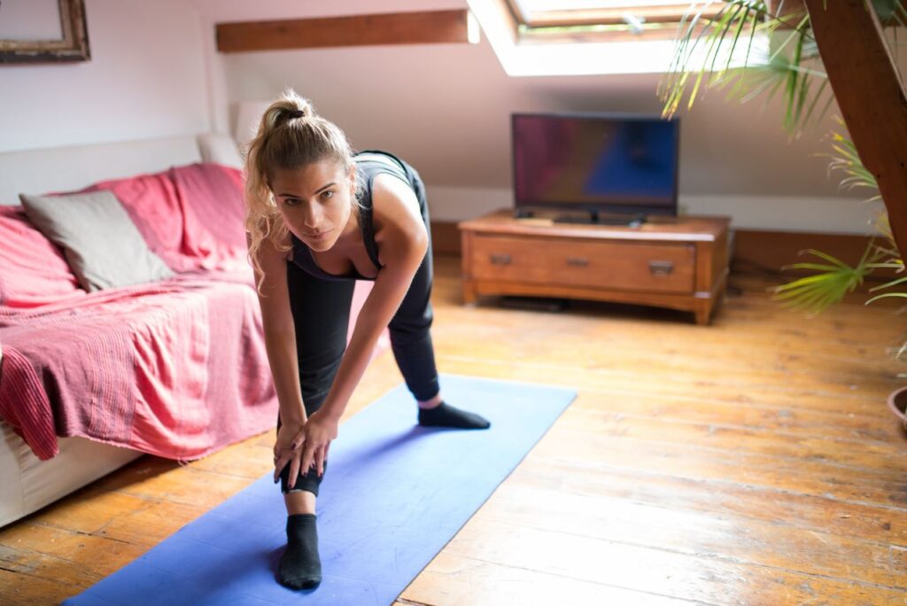 como começar bem o dia - pessoa se alongando em um tapete de yoga na sala de estar iluminada pelo sol