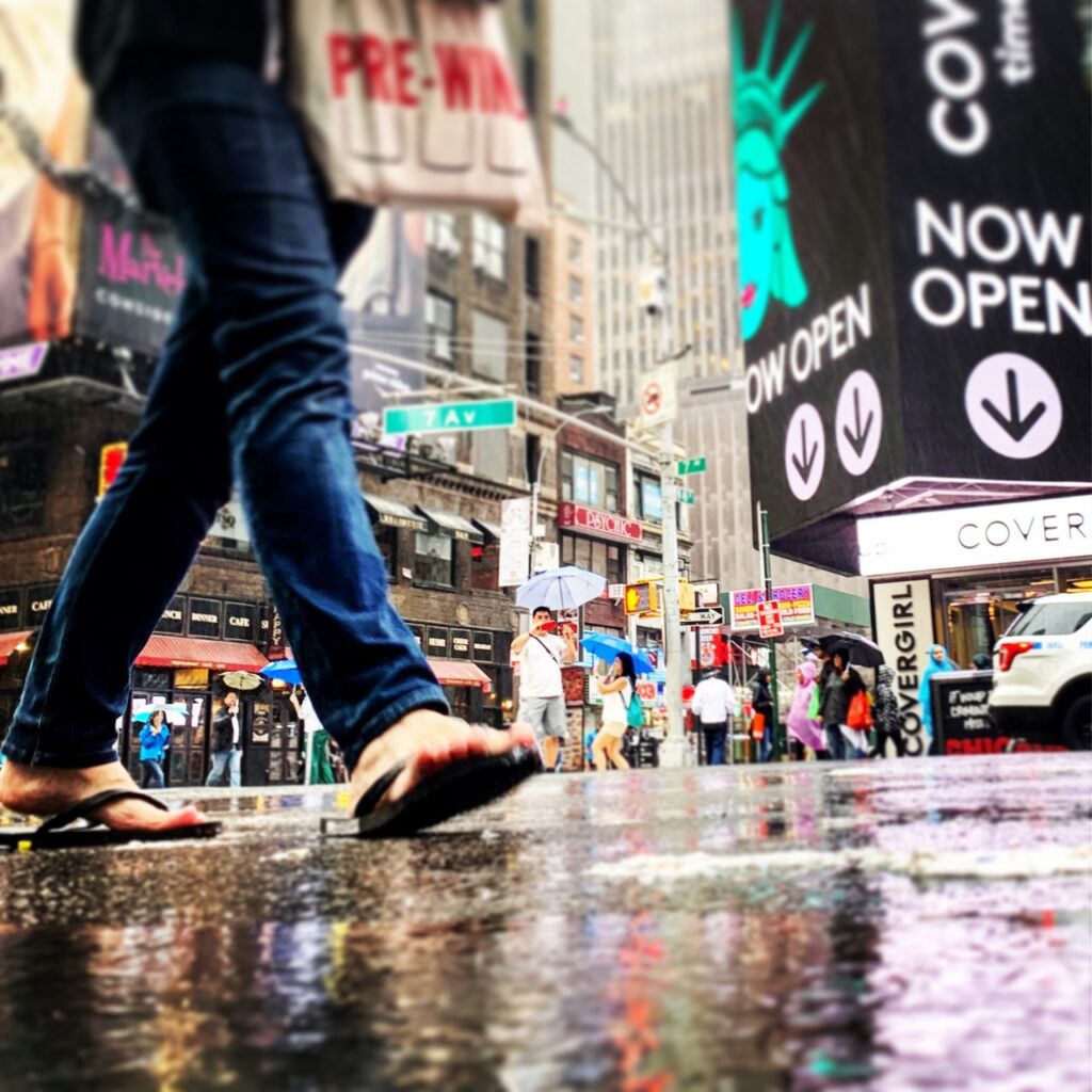 a acao cura o medo - Um close-up dramático e desfocado nos pés e sapatos de uma pessoa dando o primeiro passo para frente em uma rua urbana movimentada, simbolizando o início de uma nova jornada