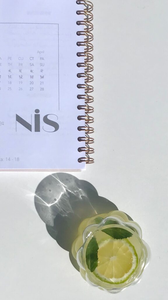 como começar bem o dia - copo de água com limão ao lado de um caderno aberto e uma caneta sobre uma mesa de madeira iluminada pela luz matinal