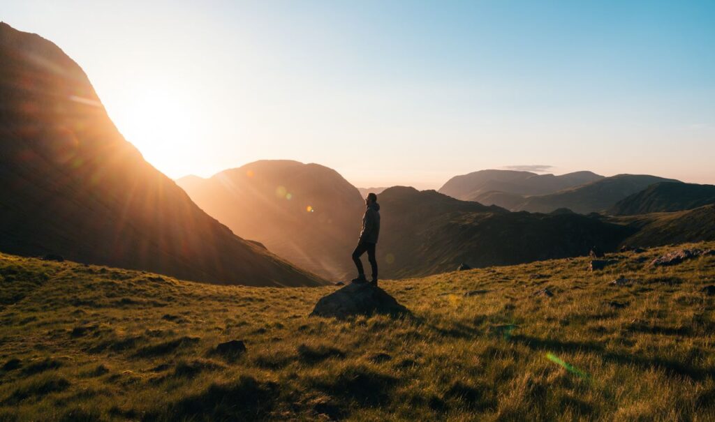 frase motivacional curta - pessoa em pé no topo de uma colina ou vista de perfil diante de uma paisagem serena ao amanhecer, com iluminação natural suave