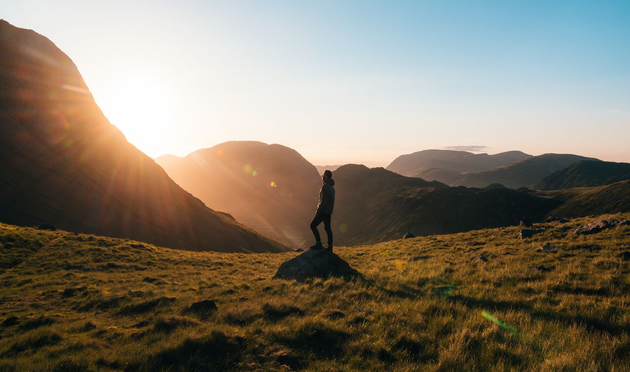 frase motivacional curta - pessoa em pé no topo de uma colina ou vista de perfil diante de uma paisagem serena ao amanhecer, com iluminação natural suave