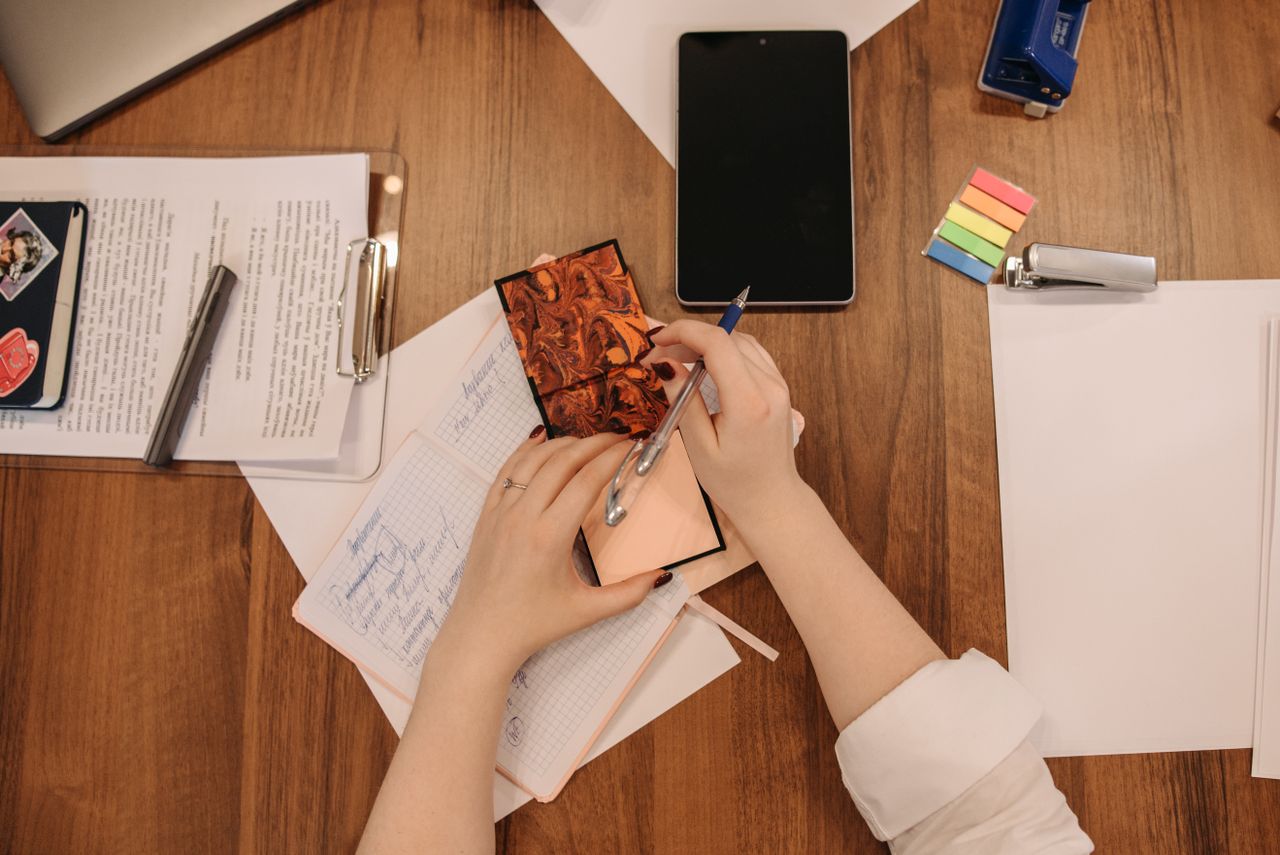 citações motivacionais - Mãos segurando uma caneta e escrevendo em um bloco de notas estético ou livro aberto em uma mesa organizada