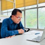 Reinvenção Profissional Após os 40 e 50 Anos - profissional de meia-idade sorrindo com postura confiante em frente a um laptop ou em uma sala de reuniões iluminada