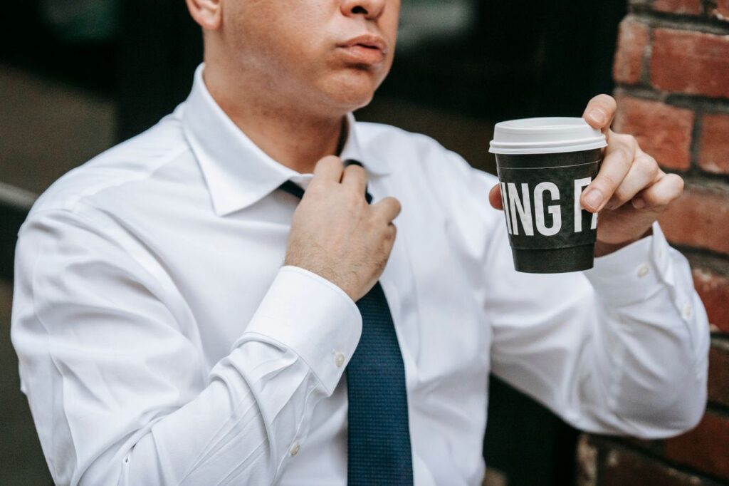 espetaculo corporativo - trabalhador afrouxando a gravata ou tirando o terno, olhando pela janela do escritório enquanto segura uma xícara de café